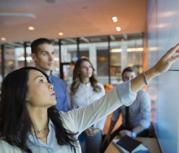 Group of coworkers in conference room having discussion with woman pointing at screen