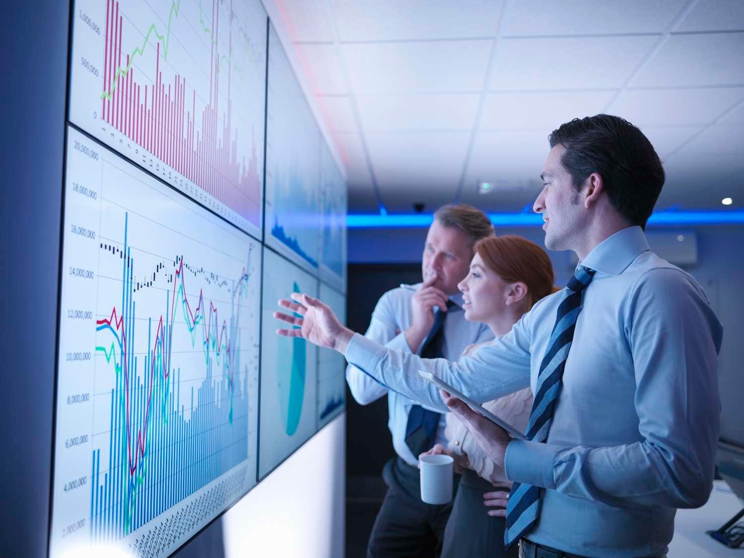 three business people discussing graphs on screen in meeting room