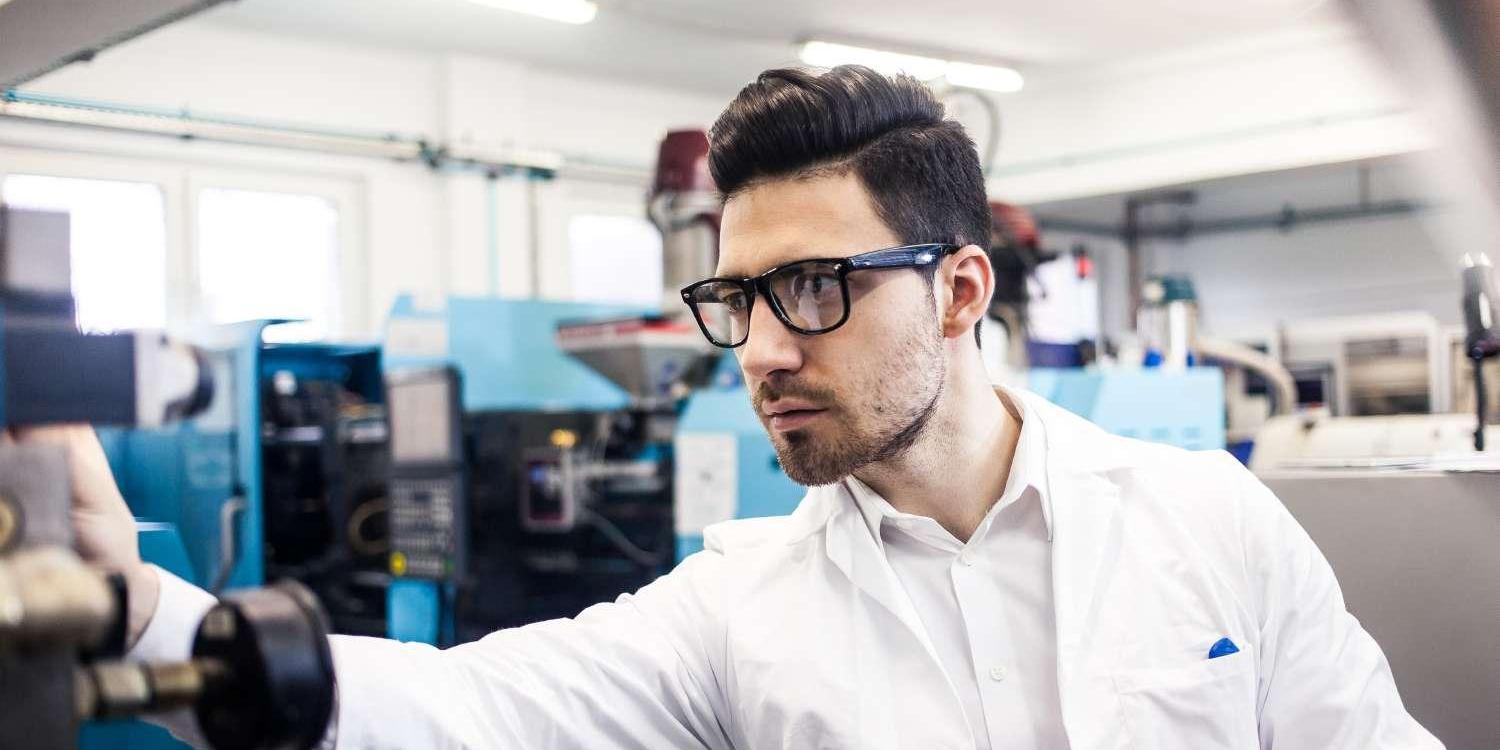 Male Engineer With Glasses and White Shirt Holding Tablet in Factory Workshop Male Engineer With Glasses and White Shirt Holding Tablet in Factory Workshop