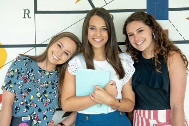 Three young female SAS employees smiling and posing in front of artwork