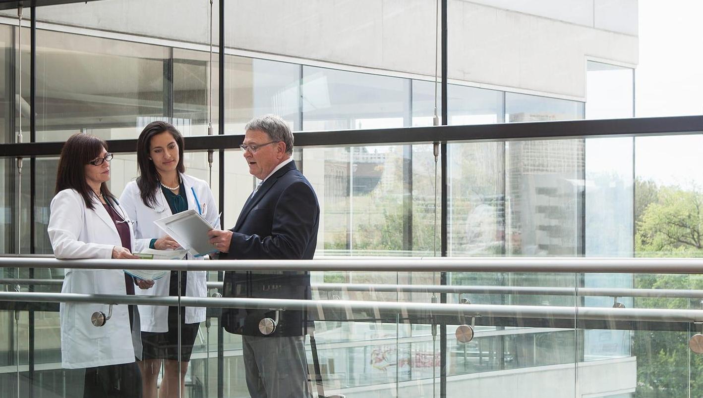 Male pharmaceutical representative with two female doctors looking at report in medical facility skywalk area