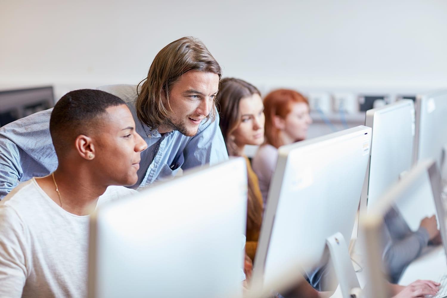 Teacher and three students in classroom reviewing data on laptops