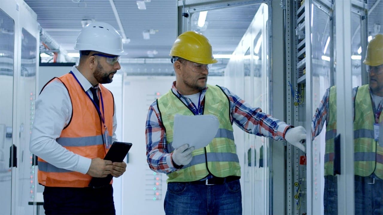 Two people in hard hats and vests discussing operations