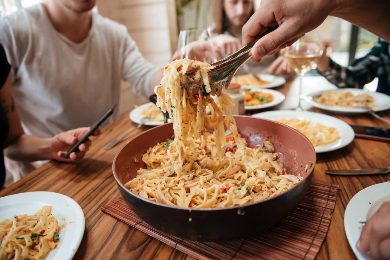 People eating pasta at a kitchen table People eating pasta at a kitchen table