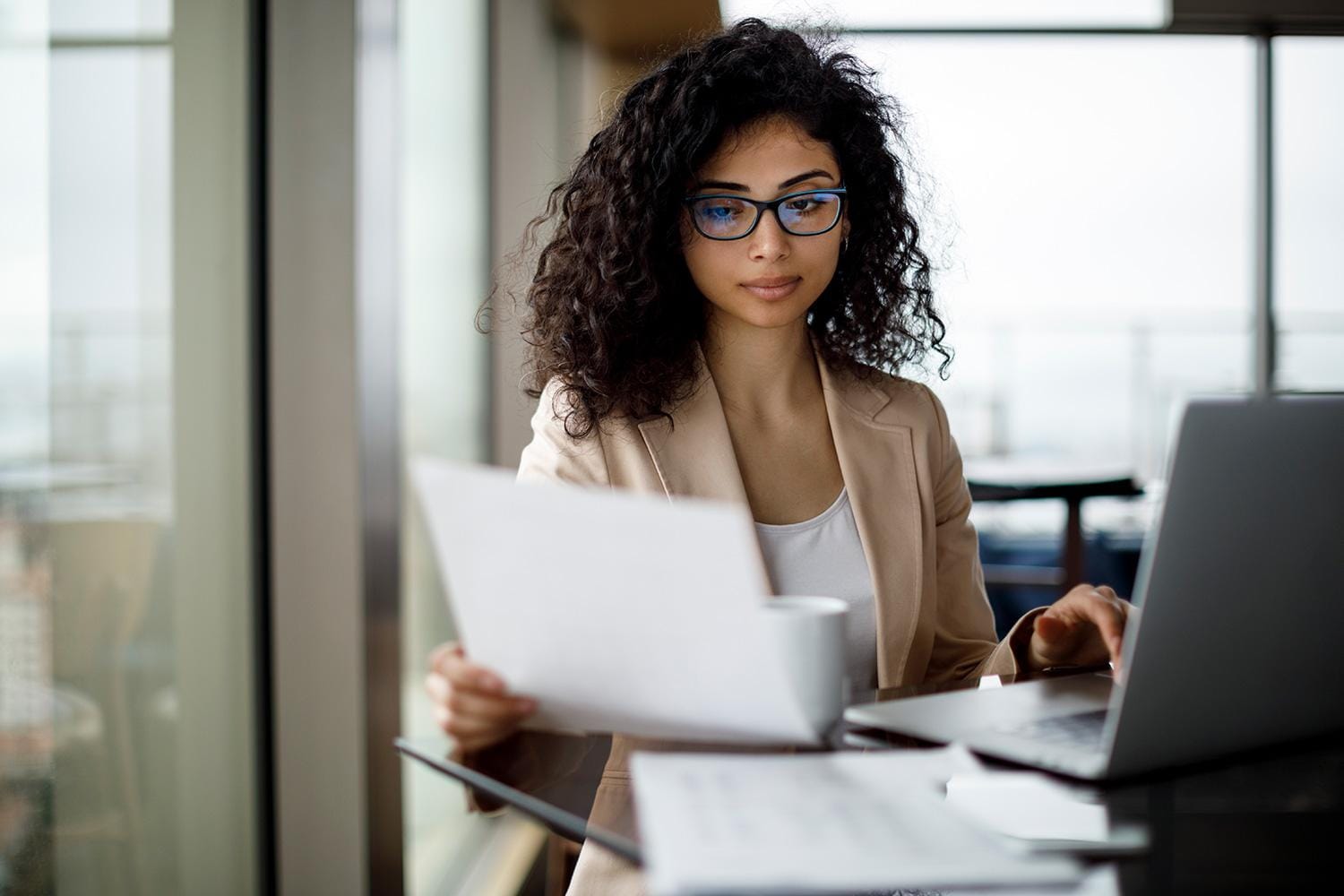 Woman holding paperwork working on laptop