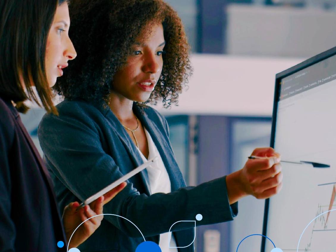 Two female coworkers viewing chart on desktop monitor